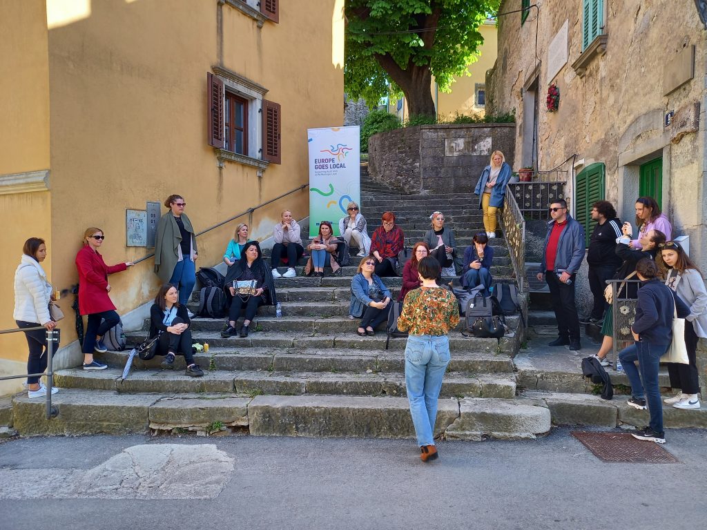 People are standing and sitting on stairs in a street