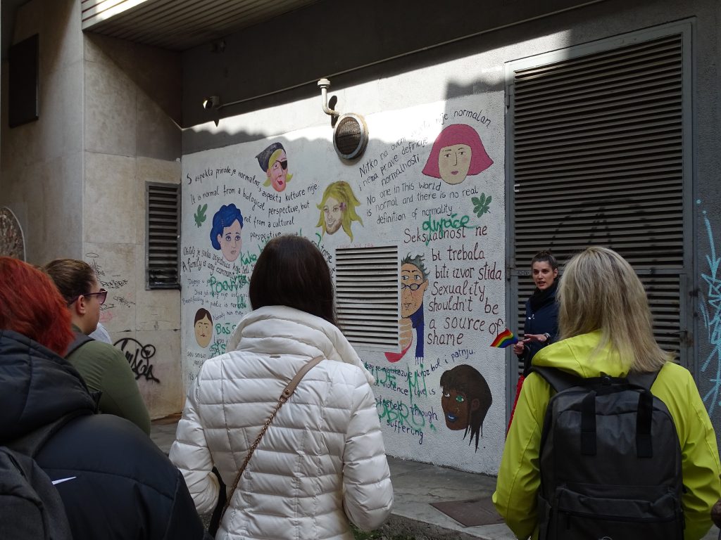 People are watching a poster with drawings of a variety of people and text